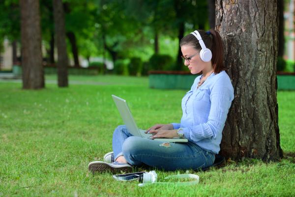 A young woman sits outside with her laptop studying one of the best online college degrees