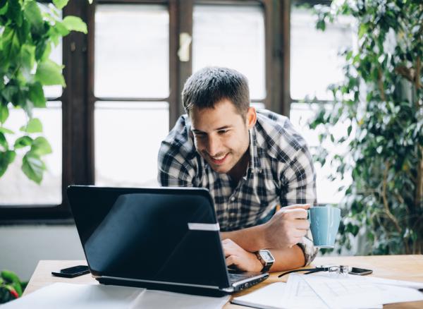 A young man smiles while drinking coffee and enjoying a positive student experience with his online college